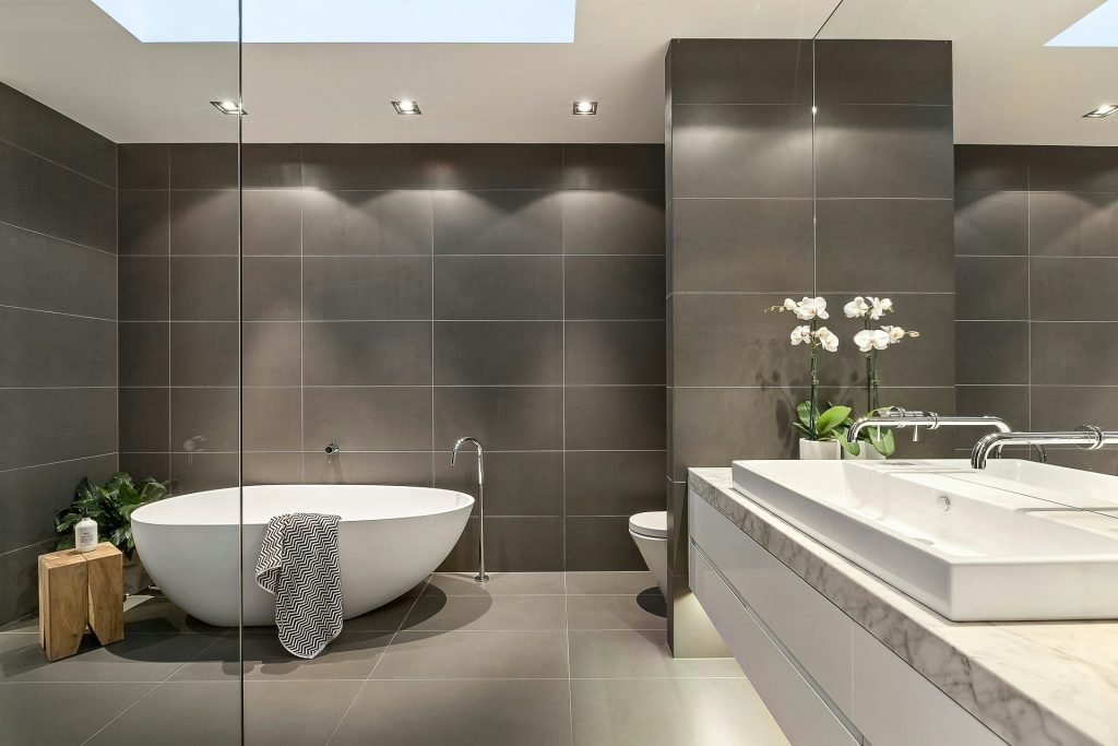Modern bathroom design featuring a freestanding white bathtub, sleek double sink with marble countertop, and elegant orchid decorations, emphasizing quality craftsmanship and contemporary aesthetics.