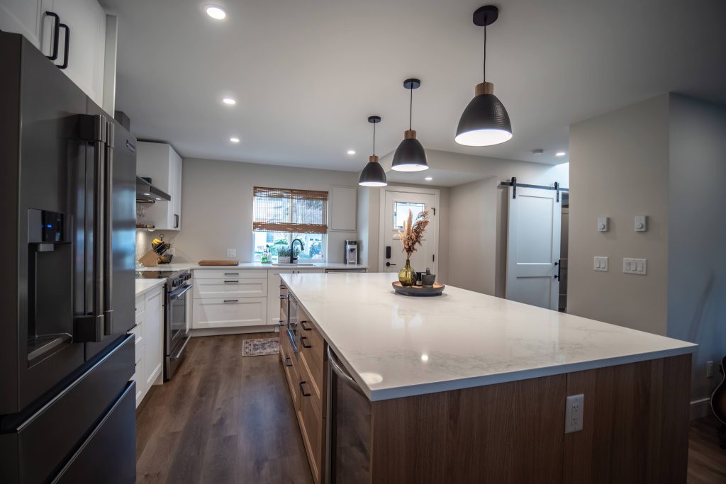Modern kitchen interior featuring a large island with quartz countertop, stainless steel appliances, and pendant lighting, showcasing DMC Contracting's quality craftsmanship in custom home design.