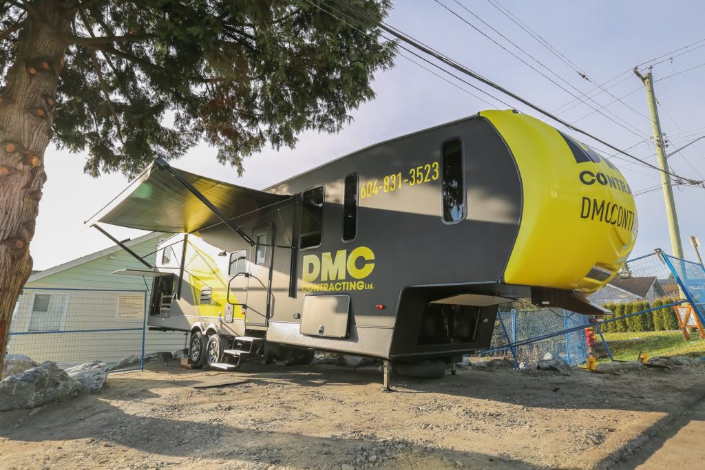 DMC Contracting mobile office trailer in Abbotsford, showcasing branding and contact information, set against a construction site backdrop.