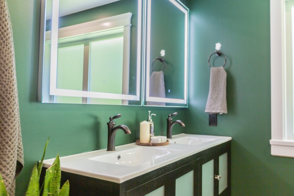 Modern bathroom design featuring a dual sink vanity with dark cabinetry, stylish faucets, and illuminated mirrors against a green wall, emphasizing functionality and aesthetics for a stylish retreat.