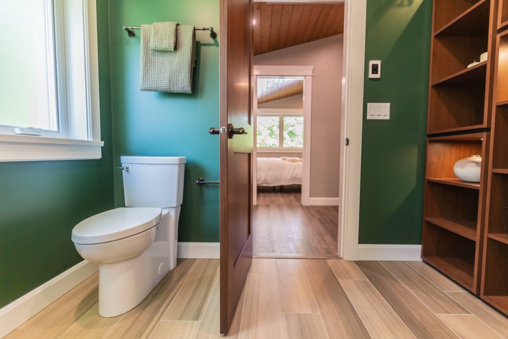 Modern bathroom interior featuring a white toilet, green walls, and natural light from a nearby window, showcasing stylish design elements relevant to DMC Contracting's renovation services.