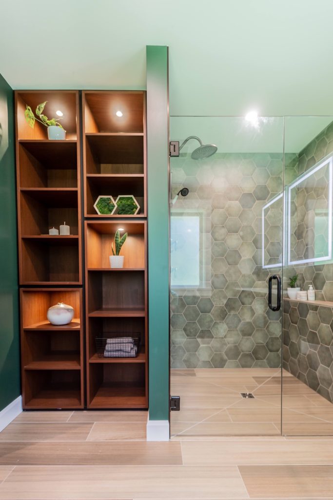 Modern bathroom design featuring a stylish shower with glass enclosure, hexagonal tiles, and a wooden storage unit with plants and decorative elements, emphasizing functionality and aesthetics in a renovated space.