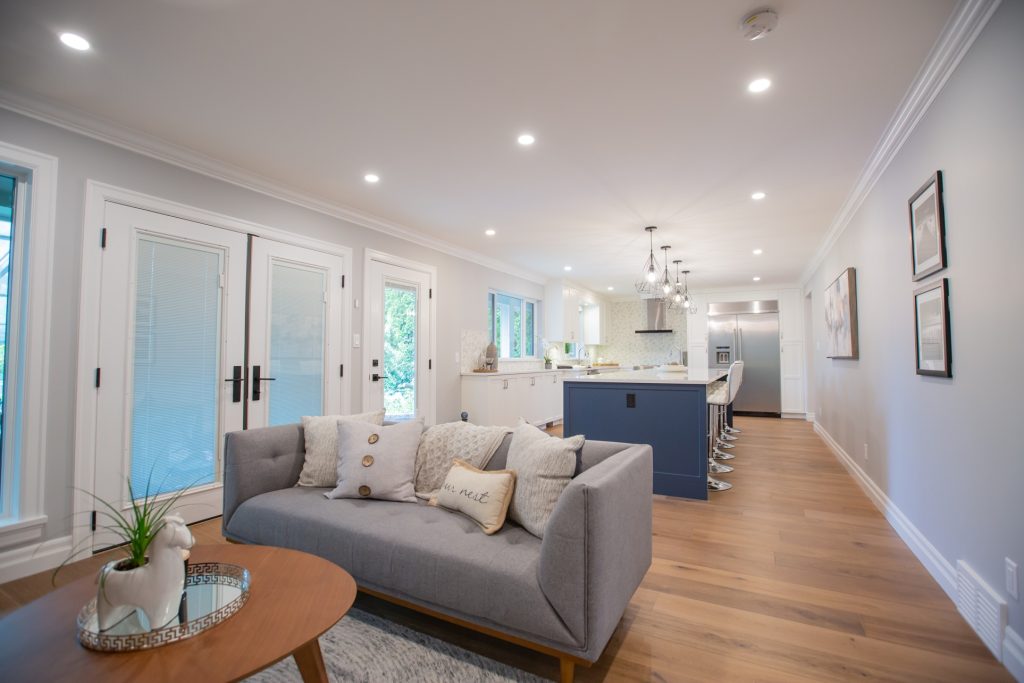 Modern open-concept living space featuring a stylish gray sofa with decorative pillows, a round coffee table, and a contemporary kitchen with bar stools, emphasizing home renovations in Fraser Valley.
