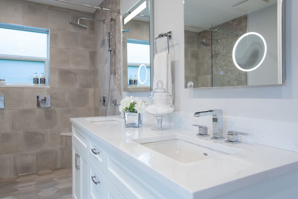 Modern bathroom renovation featuring a sleek white vanity with dual sinks, stylish faucets, decorative flowers, and contemporary lighting, showcasing a clean and functional design ideal for Fraser Valley clients.