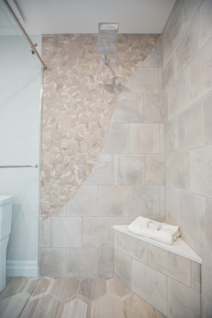 Luxury bathroom renovation featuring modern tile design, elegant pebble accent wall, and stylish showerhead, showcasing high-end finishes and custom design solutions.