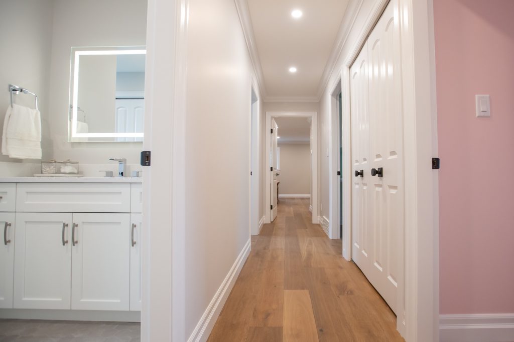 Modern hallway featuring luxury finishes, including hardwood flooring, white cabinetry, and a lighted mirror, highlighting elegant design in a home renovation context.
