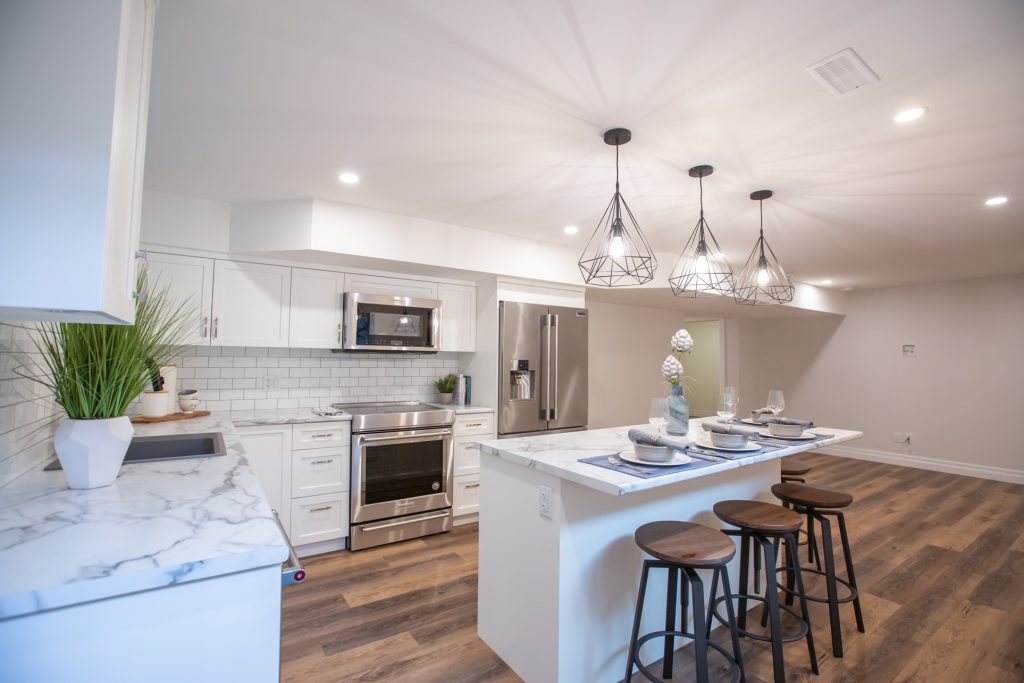 Modern kitchen interior featuring white cabinetry, stainless steel appliances, marble countertops, and decorative pendant lighting, designed for home renovations in the Fraser Valley.