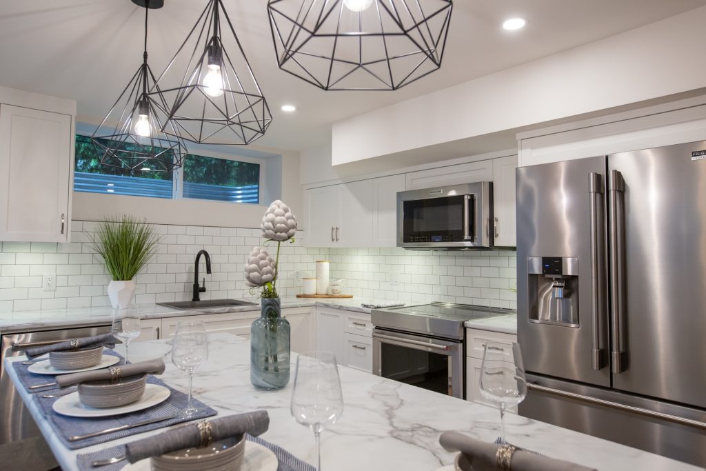 Modern kitchen featuring high-end finishes, marble countertop, stylish pendant lighting, and elegant table setting with plates and glasses, reflecting luxury home renovation by DMC Contracting in Langley and Abbotsford.