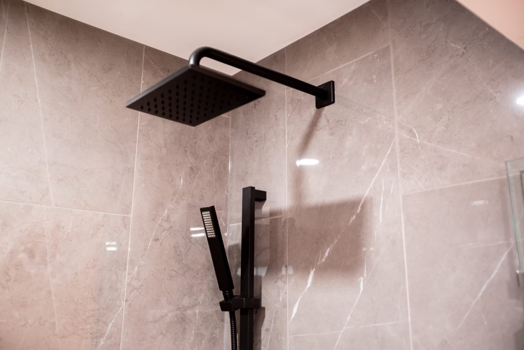 Luxury bathroom shower fixture with modern black overhead rain showerhead and handheld sprayer against elegant marble wall, showcasing high-end design elements for a sophisticated renovation.