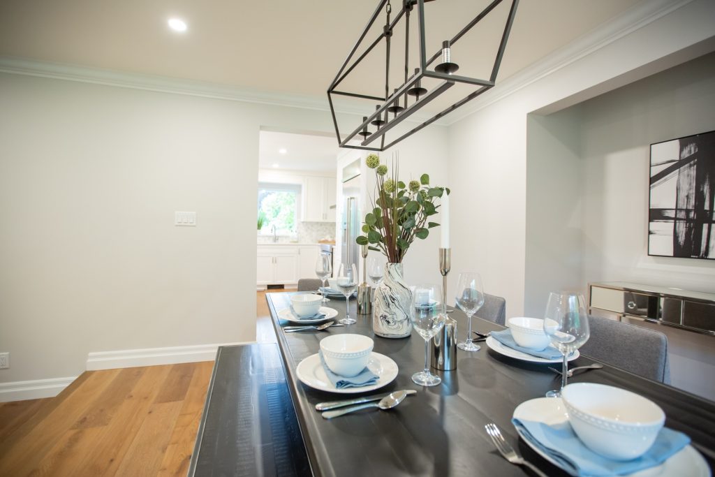 Modern dining table set for a kitchen renovation, featuring elegant tableware, decorative vase with greenery, and a view into a contemporary kitchen space, emphasizing functionality and design.
