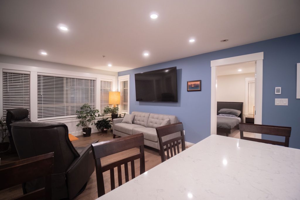 Modern living room with a gray sofa, wall-mounted TV, and stylish lighting, showcasing open layout and contemporary design elements ideal for whole home renovations by DMC Contracting in Abbotsford.