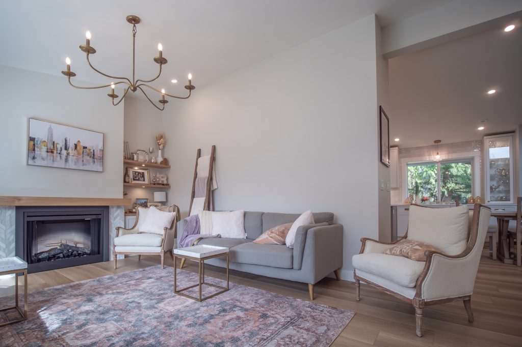 Modern living room with stylish furnishings, featuring a gray sofa, elegant chandelier, decorative artwork, and a cozy fireplace, emphasizing contemporary design and comfort for home renovation in Abbotsford.