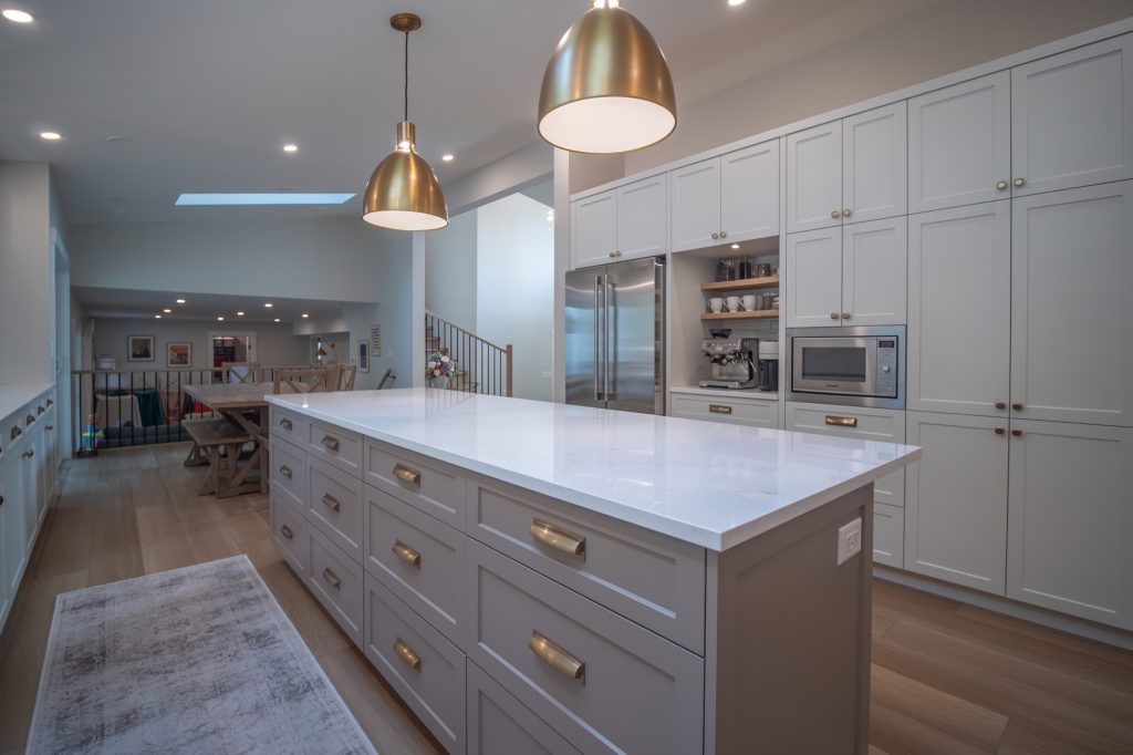 Modern kitchen renovation featuring a large island with white countertop, gold pendant lights, sleek cabinetry, and stainless steel appliances, designed for functionality and style in a home setting.