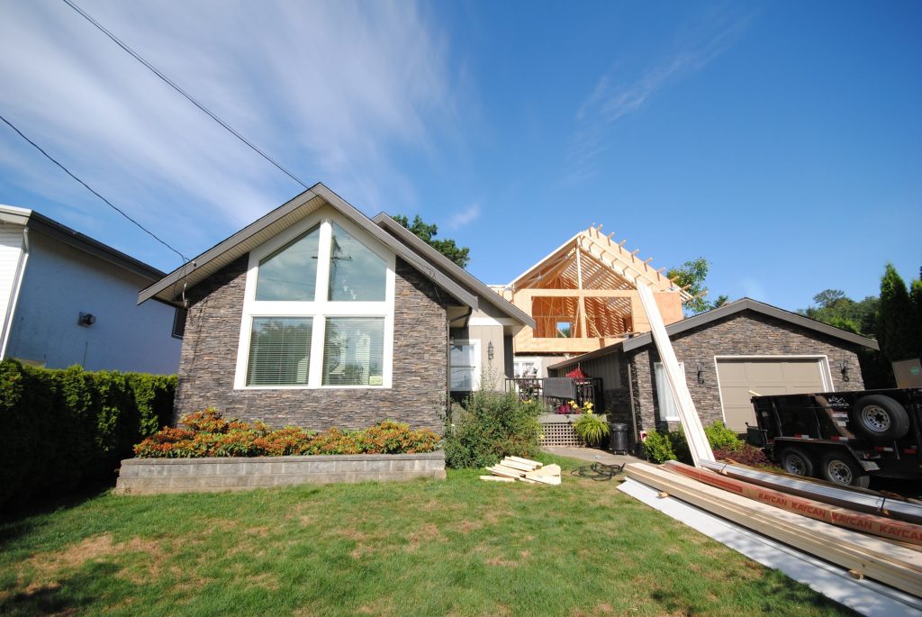 Home renovation project showcasing a multi-generational house with new construction elements, featuring a large front window, landscaped yard, and construction materials, emphasizing family living solutions in Langley and Abbotsford.